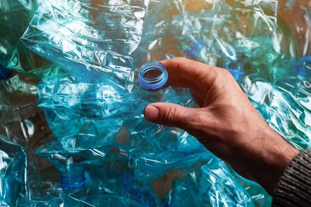 Hand among crushed plastic bottles, environmental damage concept - Фото, изображение