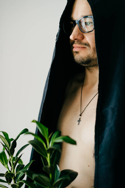 man in glasses and black ceremony cloak holding pot with green plant - Foto, imagen