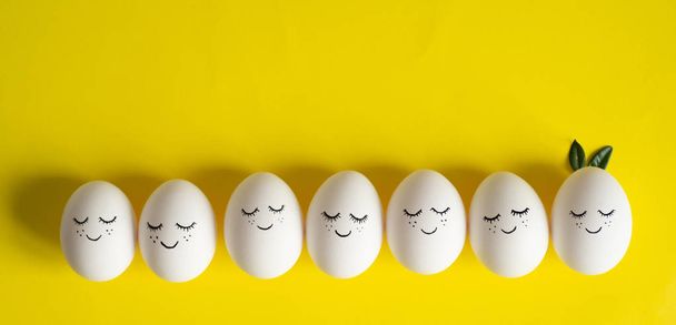 Feliz tarjeta de Pascua. Bonitos huevos de Pascua con una cara pintada en hojas de primavera sobre fondo amarillo. Feliz Pascua
 - Foto, Imagen