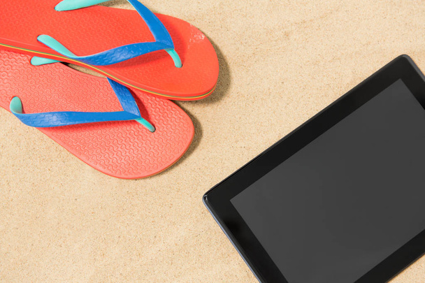 tablet computer and flip flops on beach sand - Фото, изображение