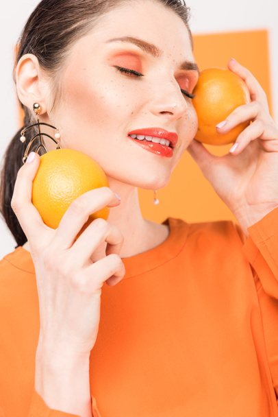 szép stílusos nő csukott szemmel tartja a narancs, és pózol a kurkuma, a háttér - Fotó, kép