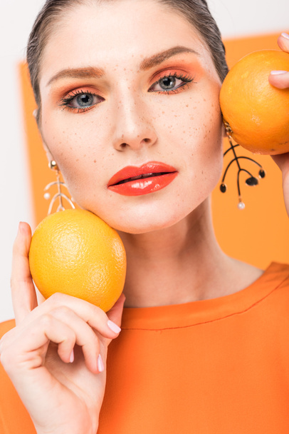 beautiful stylish woman holding oranges, looking at camera and posing with turmeric on background - Fotó, kép