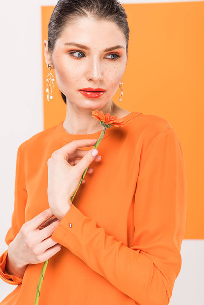 beautiful young woman holding flower, looking away and posing with turmeric on background - Photo, Image