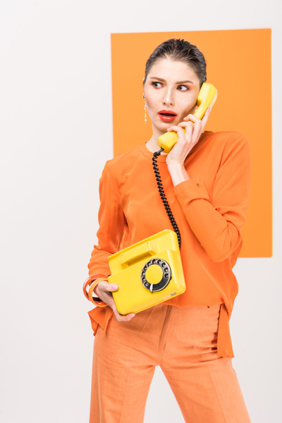 surprised fashionable young woman talking on retro telephone and posing with turmeric on background - Foto, imagen