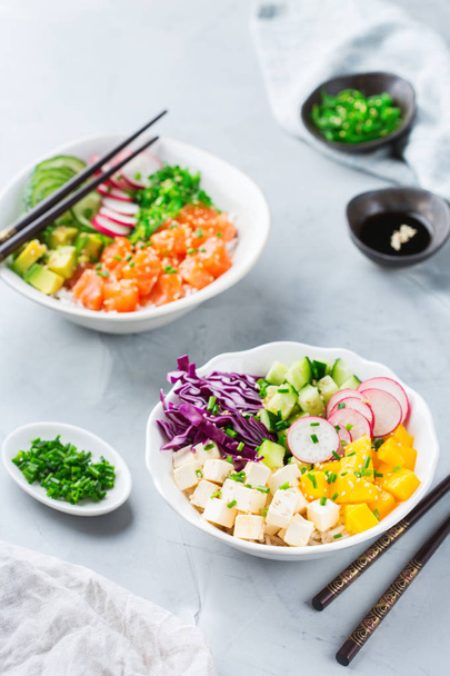 Snel en gezond eten, lunch, voeding concept. Verse biologische hawaiian zalm en tofu porren kom met rijst, zeewier, avocado, komkommer, mango op een moderne keukentafel - Foto, afbeelding