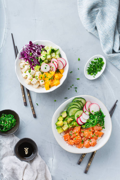 Fast and healthy food, lunch, nutrition concept. Fresh organic hawaiian salmon and tofu poke bowl with rice, seaweed, avocado, cucumber, mango on a modern kitchen table. Top view flat lay background - 写真・画像