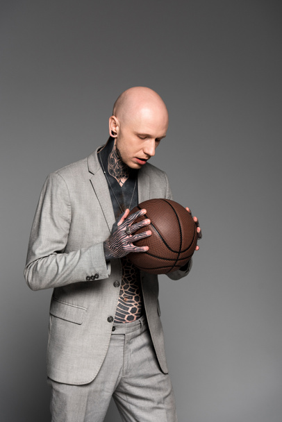 serio uomo pelato tatuato in tuta con palla da basket isolata su grigio
 - Foto, immagini