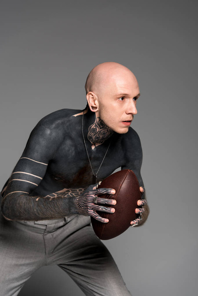 koncentrált félmeztelen férfi tetoválás, rögbi labdát gazdaság, és keres el elszigetelt szürke  - Fotó, kép