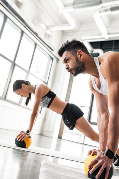 мускулистый молодой человек и спортивная девушка, занимающаяся с медицинскими шариками на ковриках для йоги
 - Фото, изображение