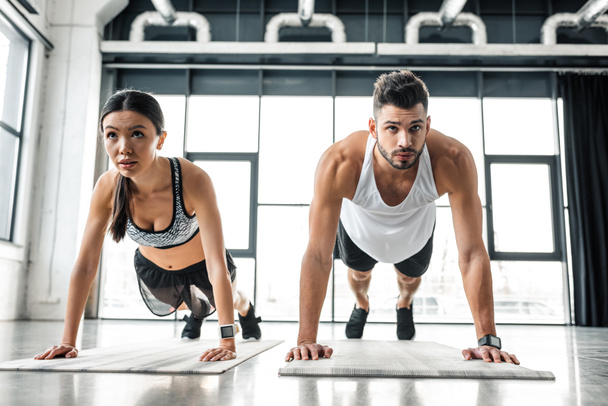 concentrated sporty young couple doing push ups on yoga mats in gym - Photo, Image