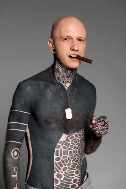 confident bare-chested man with tattoos smoking cigar and looking at camera isolated on grey - Fotoğraf, Görsel