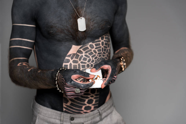 mid section of bare-chested man with tattoos holding cigarette box isolated on grey - Photo, Image