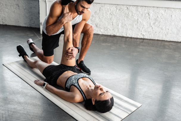 athletic young man helping sporty woman stretching on yoga mat in gym - Foto, afbeelding