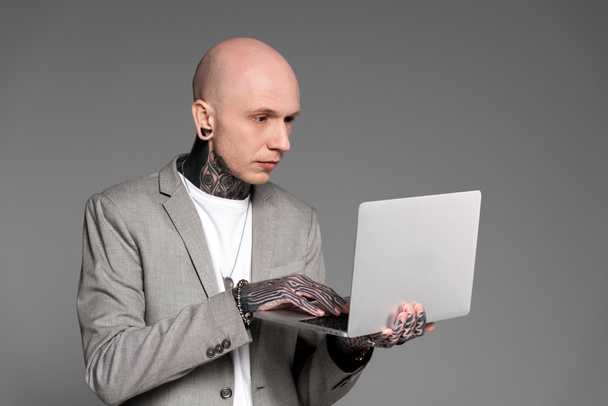 focused bald tattooed man using laptop isolated on grey - Fotoğraf, Görsel