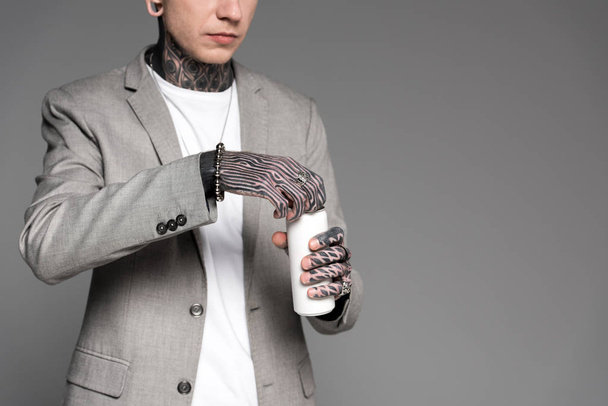 cropped shot of tattooed man in suit jacket opening aluminum can isolated on grey - Fotó, kép