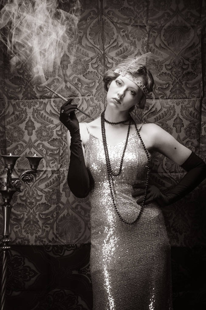 Girl in an evening dress with a cigarette mouthpiece. Studio portrait in retro style, toned in sepia - Foto, Imagem