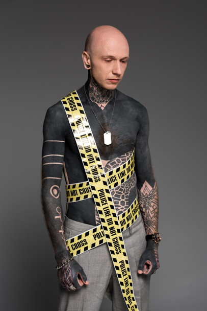 Mann mit nacktem Oberkörper, Tätowierungen und Polizeikette um den Körper, der vereinzelt auf grau herabblickt  - Foto, Bild