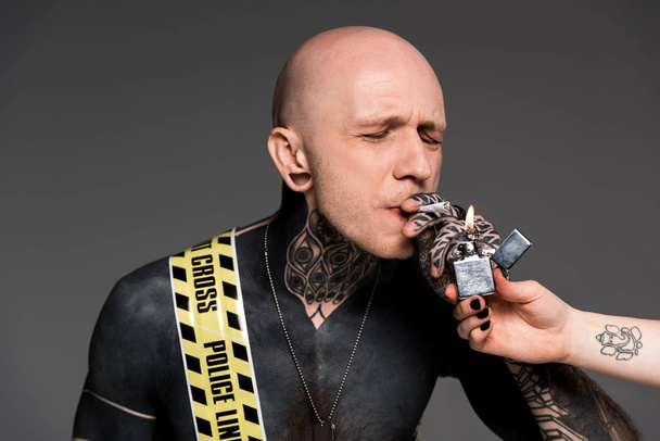 recortado disparo de alguien sosteniendo más ligero y hombre tatuado con línea cruzada alrededor del cuerpo fumar cigarrillo roll-up aislado en gris
   - Foto, Imagen