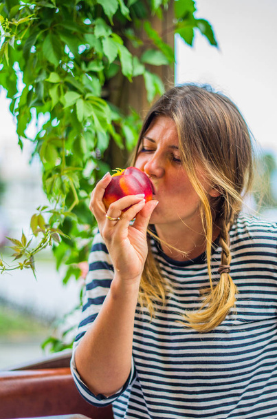 Πορτρέτο του χαριτωμένο γυναίκα τρώει ολόκληρο φρέσκο ροδάκινο - Φωτογραφία, εικόνα