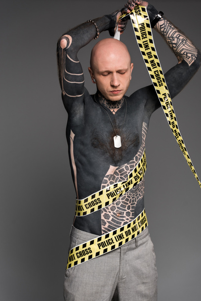 bald shirtless tattooed man wrapping himself with cross line isolated on grey - Photo, Image