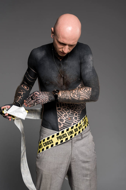 shirtless getatoeëerd man zichzelf met inwikkeling Kruis lijn geïsoleerd op grijs - Foto, afbeelding