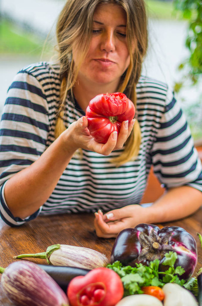 Mujer linda comiendo tomate rojo fresco entero en la mesa con verduras crudas
 - Foto, Imagen