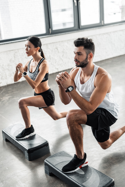 high angle view of concentrated young couple exercising on step platforms and looking away in gym - Foto, Imagen