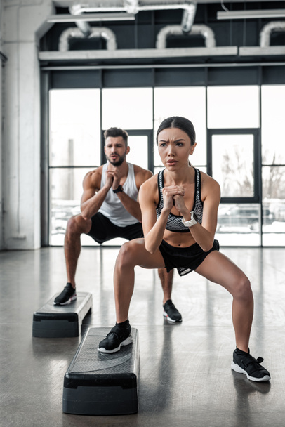 full length view of concentrated young couple exercising with step platforms in gym - Photo, Image