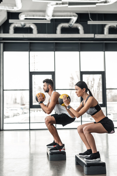 vista laterale della giovane coppia atletica in allenamento di abbigliamento sportivo con piattaforme passo in palestra
 - Foto, immagini