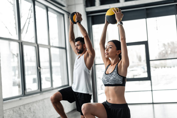 athletic young man and woman in sportswear exercising with medicine balls in gym - Фото, изображение