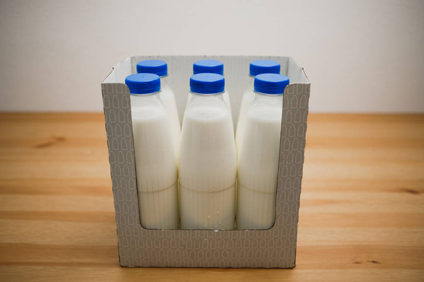 Молочные бутылки в картонной коробке на деревянном столе
 - Фото, изображение