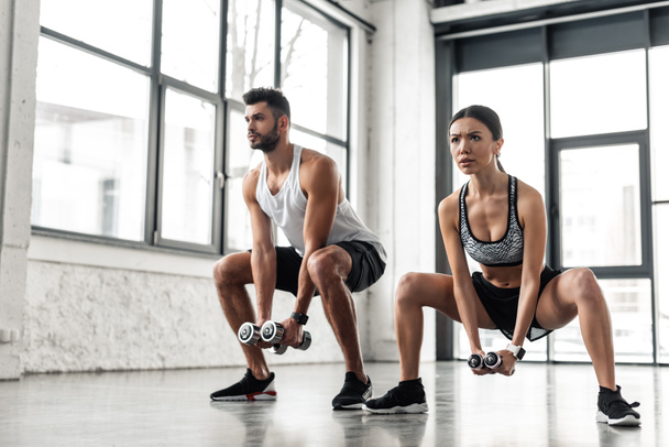 sportos fiatal férfi és nő edzőterem súlyzókkal, guggolás - Fotó, kép