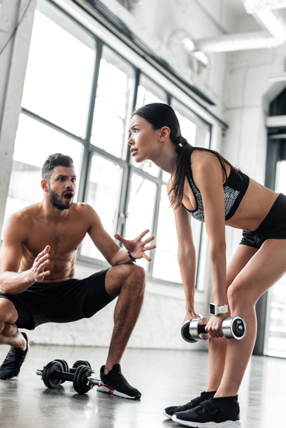 el hareketi ve sportif kız spor salonunda dumbbells ile egzersiz için konuşurken erkek eğitmen  - Fotoğraf, Görsel