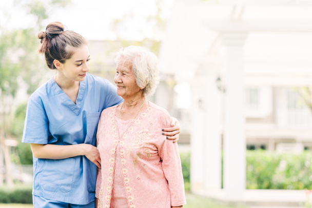 Cuidador de enfermeira sorridente com mulher idosa asiática ao ar livre no parque
 - Foto, Imagem