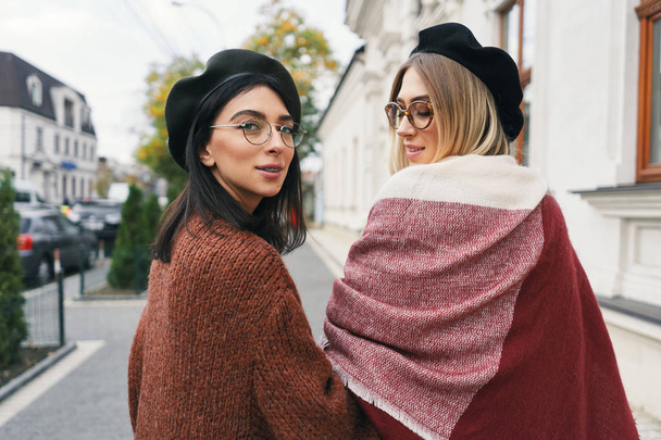 Happy moments with two stylish girls, looking over shoulder, smiling, walking on a street in the city. Closeup portrait, funny, joyful attractive young women having fun, best friends, sisters. - Photo, Image