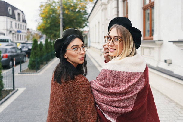 Happy moments with two stylish girls, looking over shoulder, smiling, walking on a street in the city. Closeup portrait, funny, joyful attractive young women having fun, best friends, sisters. - Photo, Image