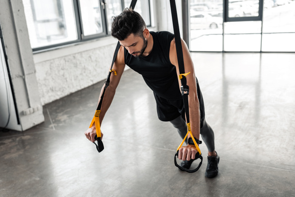 Blick aus der Vogelperspektive auf einen muskulösen jungen Mann, der mit Widerstandsbändern im Fitnessstudio trainiert - Foto, Bild