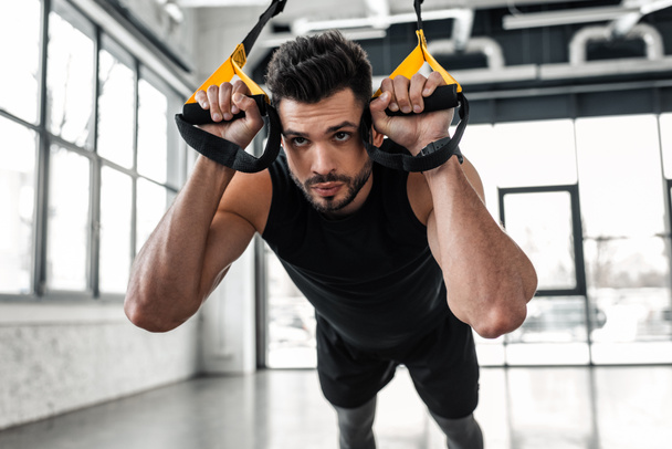 schöner, konzentrierter, sportlicher Mann hängt und trainiert mit Fitnessbändern im Fitnessstudio - Foto, Bild