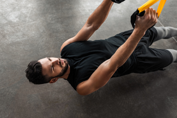 vista ad alto angolo di concentrato allenamento muscolare giovane uomo con cinghie di sospensione in palestra
  - Foto, immagini