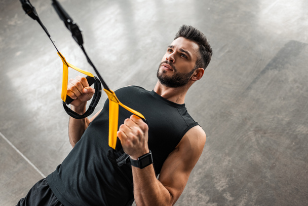 high angle view of athletic young man in sportswear hanging and training with resistance bands in gym  - Foto, Imagem