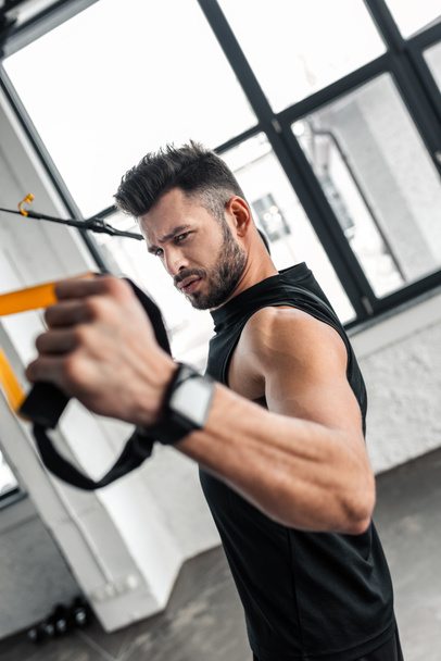 handsome serious young man exercising with suspension straps in gym - Photo, Image