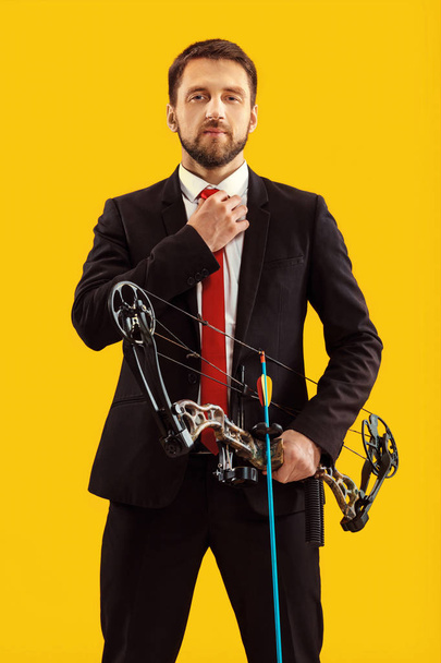 Businessman aiming at target with bow and arrow, isolated on yellow background - 写真・画像