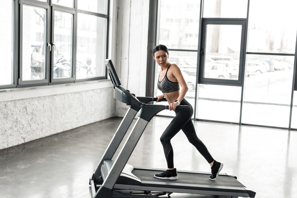 Ganzkörperansicht der sportlichen jungen Frau, die im Fitnessstudio auf dem Laufband trainiert - Foto, Bild