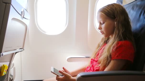 Adorable niña viajando en avión sentada cerca de la ventana. Niño escuchando música sentado cerca de la ventana del avión
 - Metraje, vídeo