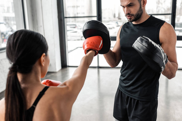 cropped shot of male trainer and young sportswoman boxing in gym - Фото, изображение