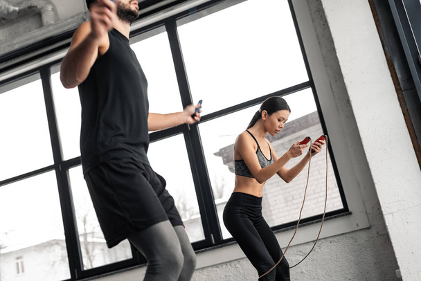περικοπεί shot νεαρό ζευγάρι εκπαίδευση με άλματα σχοινιά στο γυμναστήριο  - Φωτογραφία, εικόνα