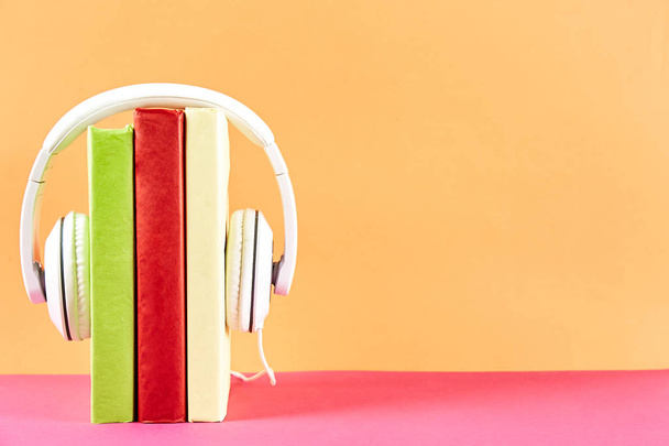 Electronic audiobook vs regular paper book concept. Stack of different color hardcover books with blank colorful covers & white headphones on table. Old versus new. Close up, copy space, background. - Foto, imagen