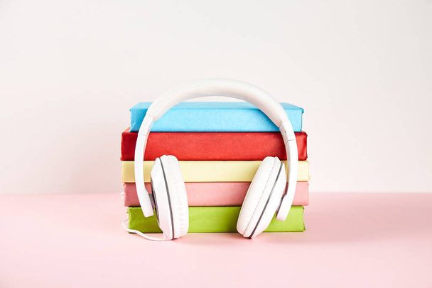 Electronic audiobook vs regular paper book concept. Stack of different color hardcover books with blank colorful covers & white headphones on table. Old versus new. Close up, copy space, background. - 写真・画像