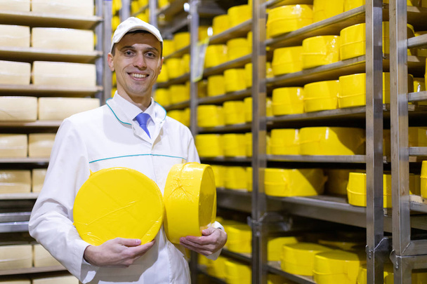 hombre sosteniendo una cabeza de queso en una planta lechera
 - Foto, imagen