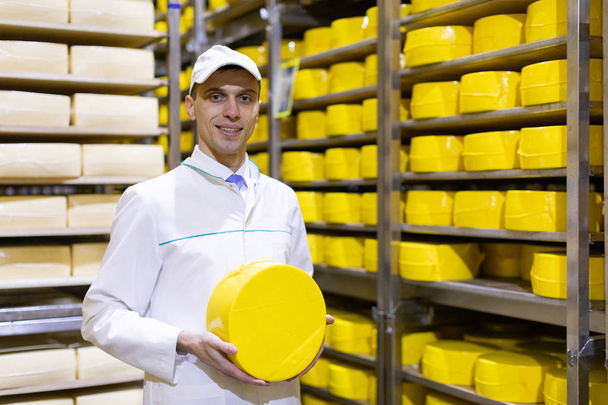 muž v bílém rouchu s hlavou sýra v jeho rukou je ve skladu sýrů - Fotografie, Obrázek